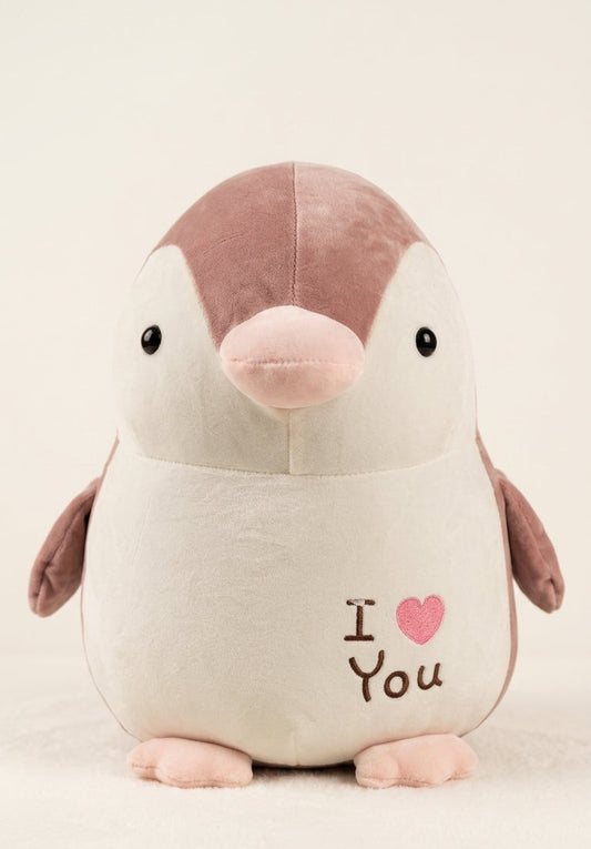 A plush penguin toy with a cream-colored body, a dusty pink crown and wings, and a light pink beak and feet. The front of the penguin is embroidered with 'I [pink heart] You' in brown thread.