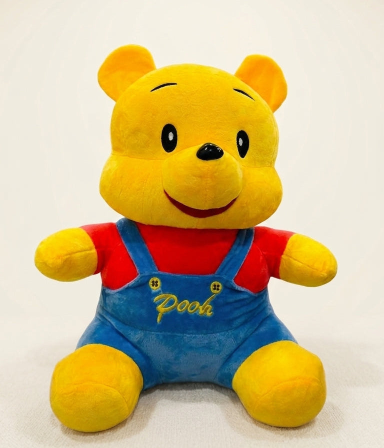 A plush toy of Winnie the Pooh sitting upright, wearing his signature red shirt and blue overalls with yellow embroidered details, set against a plain light background.