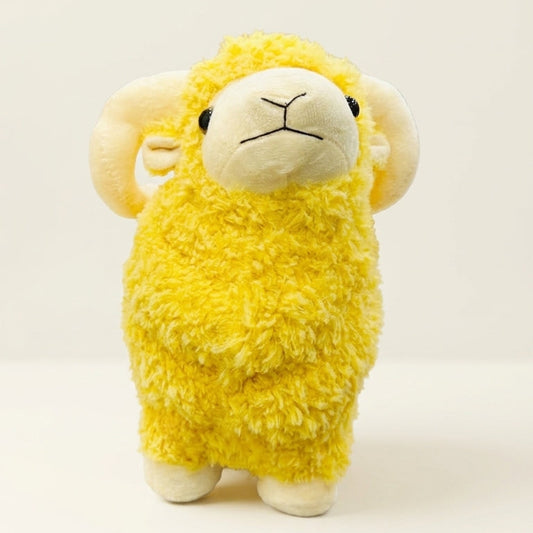 A yellow fluffy sheep plush toy with cream-colored horns, face, and feet, standing on a white surface against a light off-white background.